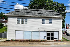 A two-story white building with a garage door, a small porch with plants, and a street view with cars and a sidewalk.