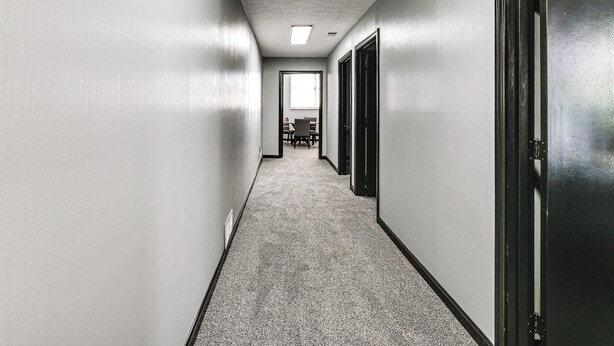 A narrow hallway with a carpeted floor, white walls, and a door on the right.