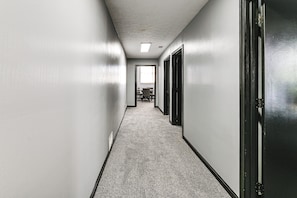 A hallway with a carpeted floor, white walls, and a door on the right.
