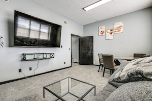 A modern room with a glass coffee table, a large flat-screen TV, a dining area with chairs, and artwork on the walls.