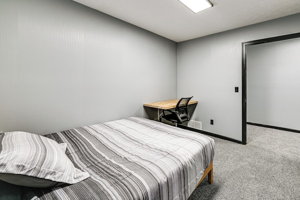 A bedroom with a bed, a desk, and a chair.