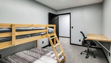 A bunk bed with a ladder, a desk with a chair, and a door in a room with grey walls and carpet.