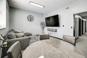 A modern living room with a round marble table, a sofa, a flat-screen TV, and a potted plant.