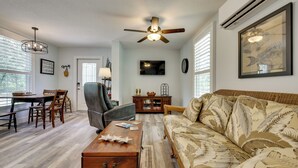 Un salon comprenant un canapé, une table basse, une table à manger avec des chaises, un ventilateur de plafond et un téléviseur fixé au mur.