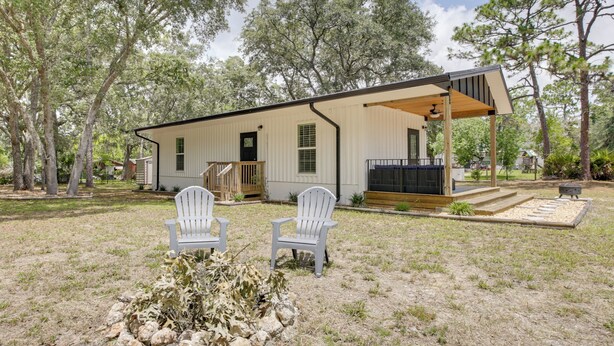 Une maison de plain-pied dotée d’un porche couvert, de deux chaises Adirondack blanches et d’un petit espace patio.