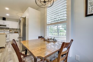 Eine moderne Küche mit weißen Schränken, einem Edelstahl-Kühlschrank, einem Holztisch und einem Fenster mit Jalousien.