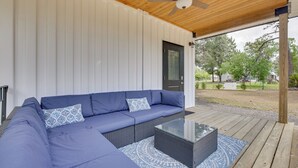 Un espace extérieur abrité, aménagé avec un canapé d’angle, une table basse en verre et un ventilateur de plafond.