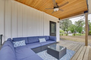 Ein überdachter Außenbereich mit einer Eckcouch, einem Couchtisch mit Glasplatte und einem Deckenventilator.