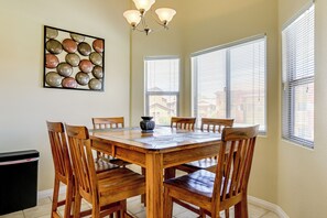 A dining area with a wooden table and chairs, a chandelier, and a wall-mounted decorative piece. - Golf & Gamble! Mesquite Condo w/ Pool Access (Mesquite)
