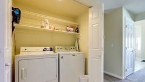 A laundry room with two washers and dryers, a shelf with cleaning supplies, and a door leading to another room. - Golf & Gamble! Mesquite Condo w/ Pool Access (Mesquite)