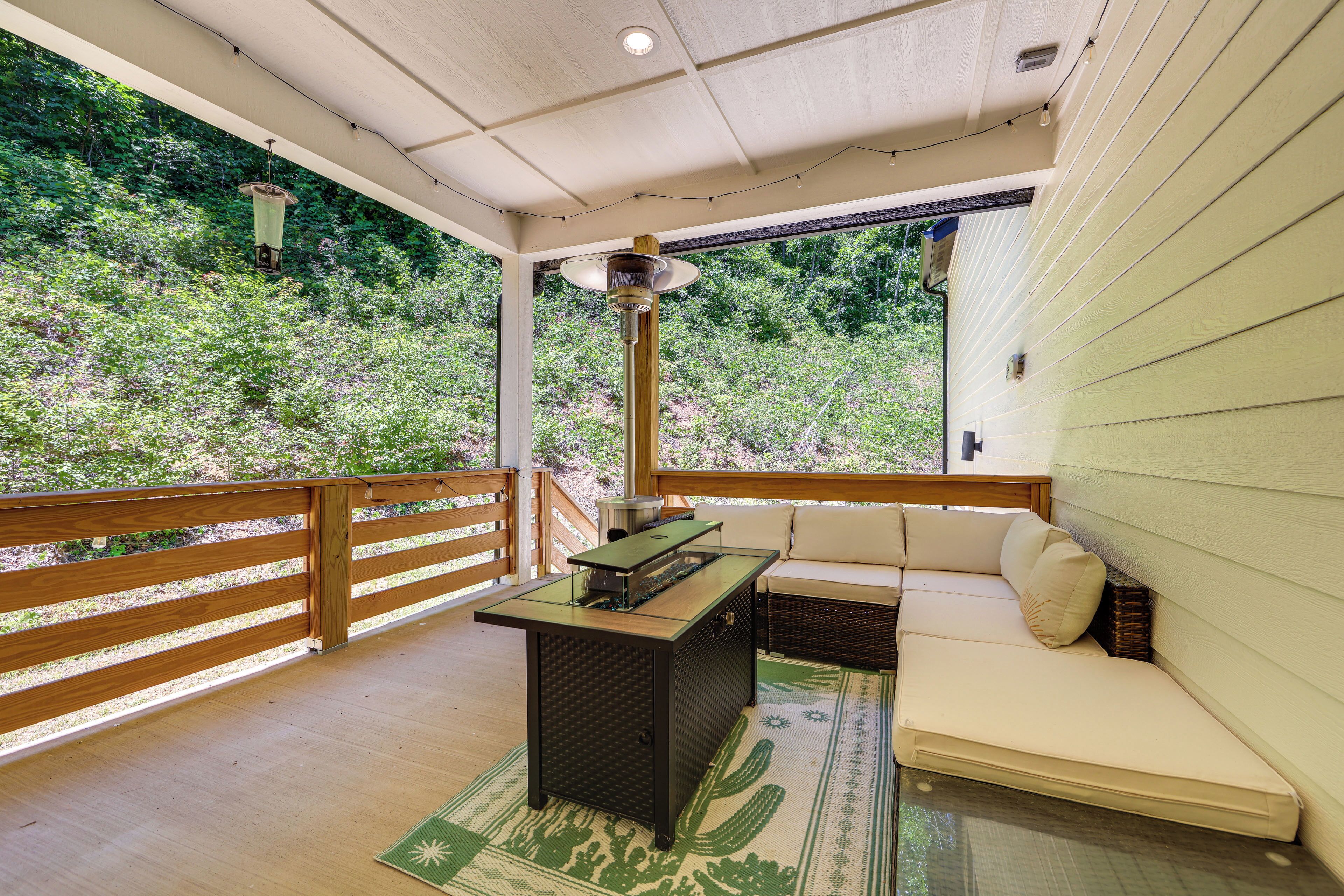 Un espace extérieur aménagé, abrité et doté d’une table en bois, d’un canapé confortable et d’un tapis orné de motifs de cactus.