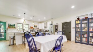 A modern kitchen with white cabinets, a dining table with blue chairs, and a bookshelf filled with books. - Deck & Fire Pit! Mtn Escape, 12 Mi to Asheville (Leicester)