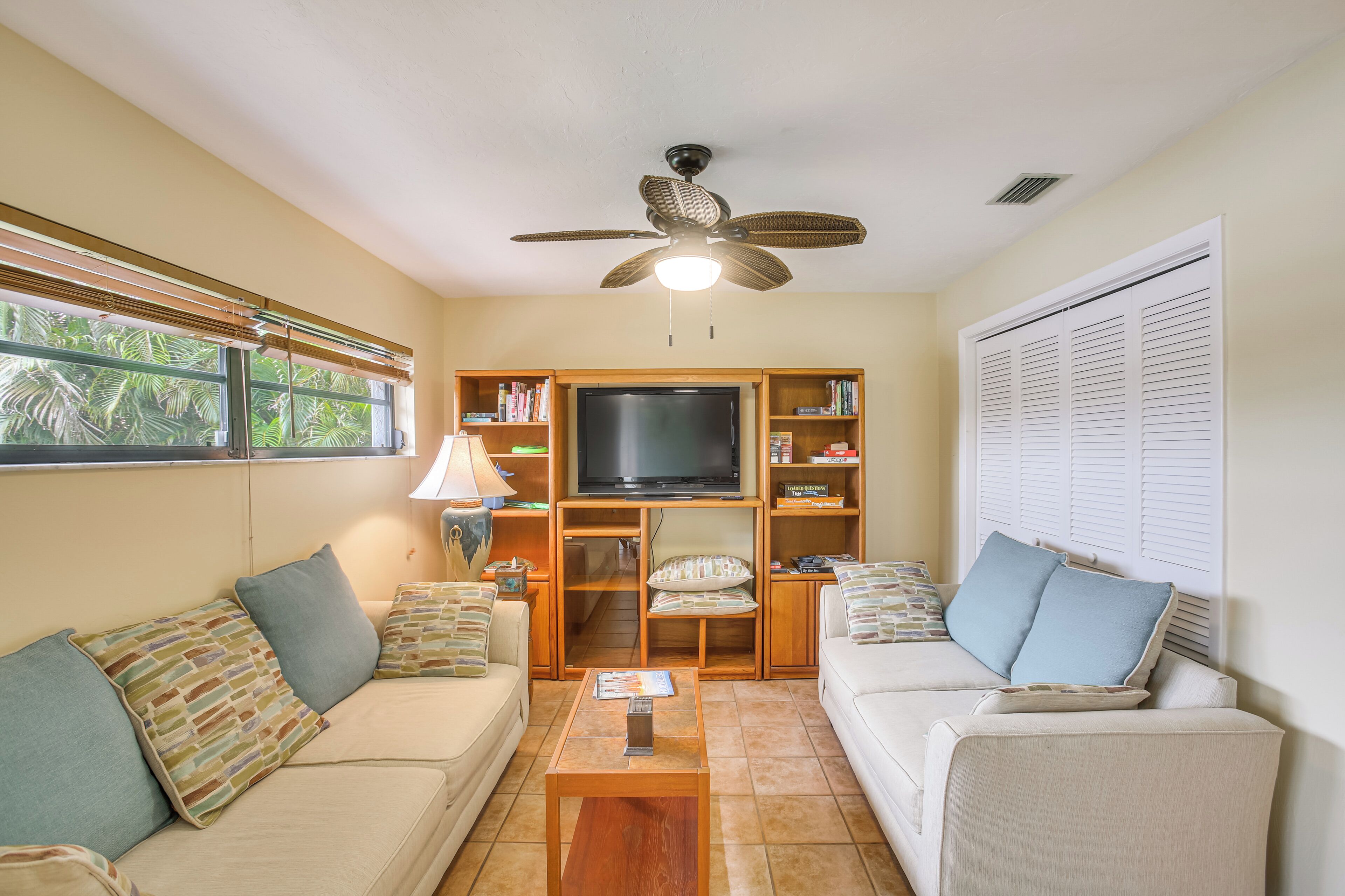 A living room with a ceiling fan, a television, two sofas, a coffee table, and a bookshelf.