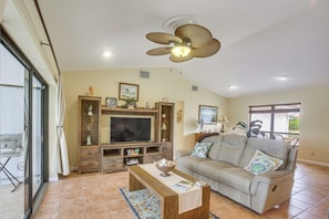 A living room with a sofa, TV, wooden entertainment center, ceiling fan, and a sliding glass door. - Canal-front Gem w/ Boat Dock! Punta Gorda Getaway (Punta Gorda)