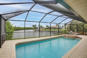 A swimming pool with a covered area, a hot tub, and a view of a residential area with palm trees. - Canal-front Gem w/ Boat Dock! Punta Gorda Getaway (Punta Gorda)