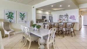 A dining area with a table and chairs, a kitchen in the background, and artwork on the walls. - 3BR Beachfront PH Suite: Suntide III - Unit 1203 (South Padre Island)