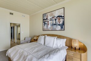 Ein Hotelzimmer mit einem großen Bett, einem Nachttisch mit Lampe, einem Bild an der Wand und einer Tür zu einem weiteren Raum.