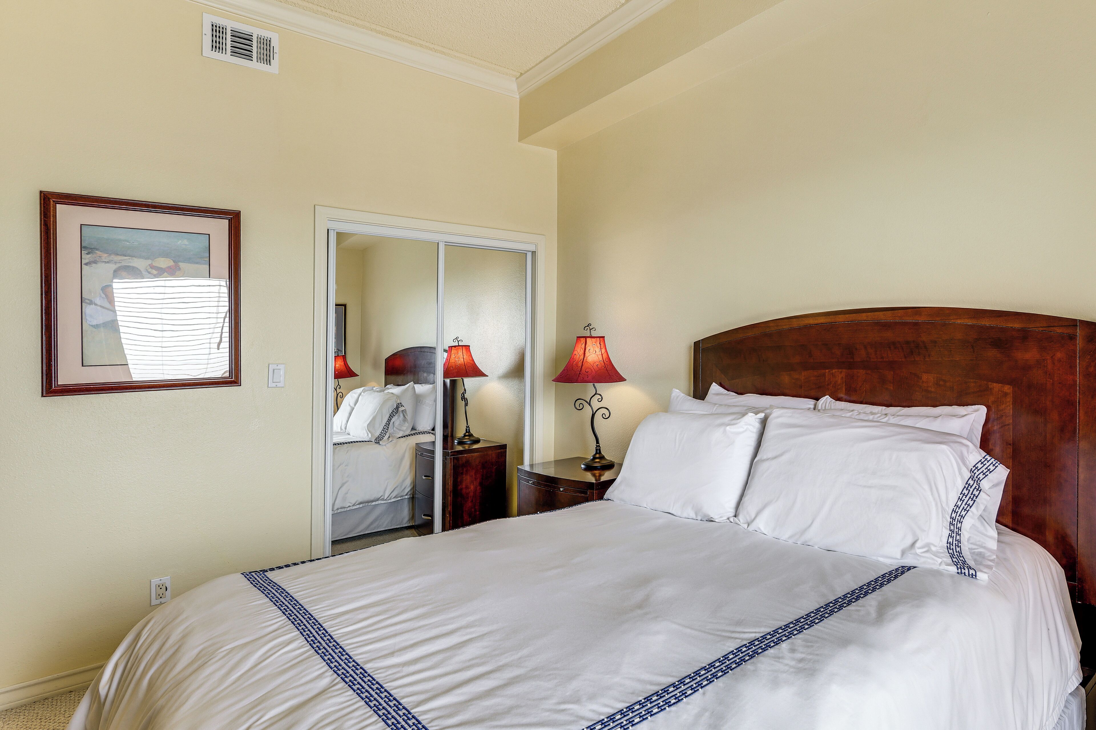 A hotel room with a large bed, two bedside tables with lamps, a mirror, and a framed picture on the wall.