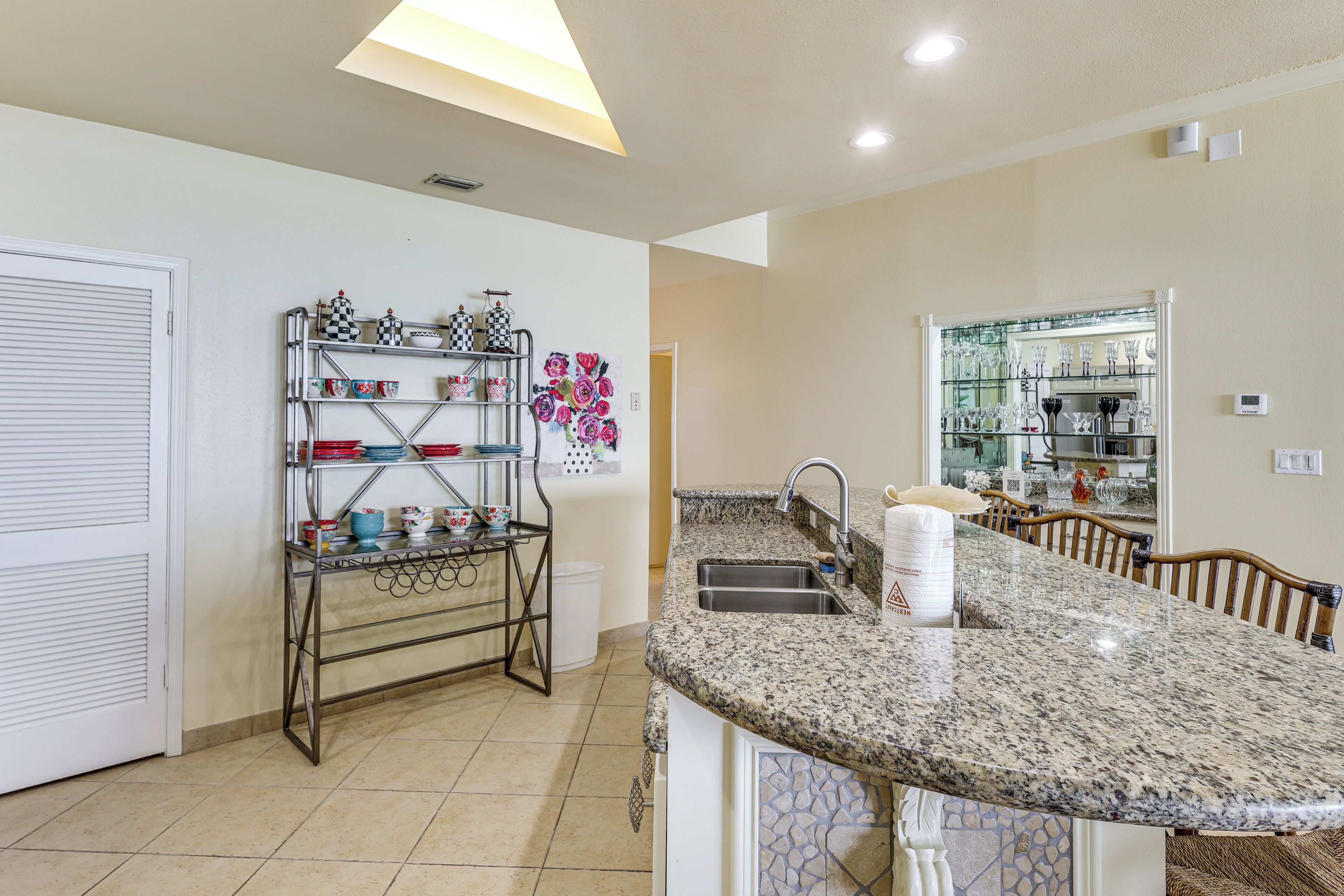 A kitchen with a granite countertop, stainless steel sink, and a metal rack with dishes.