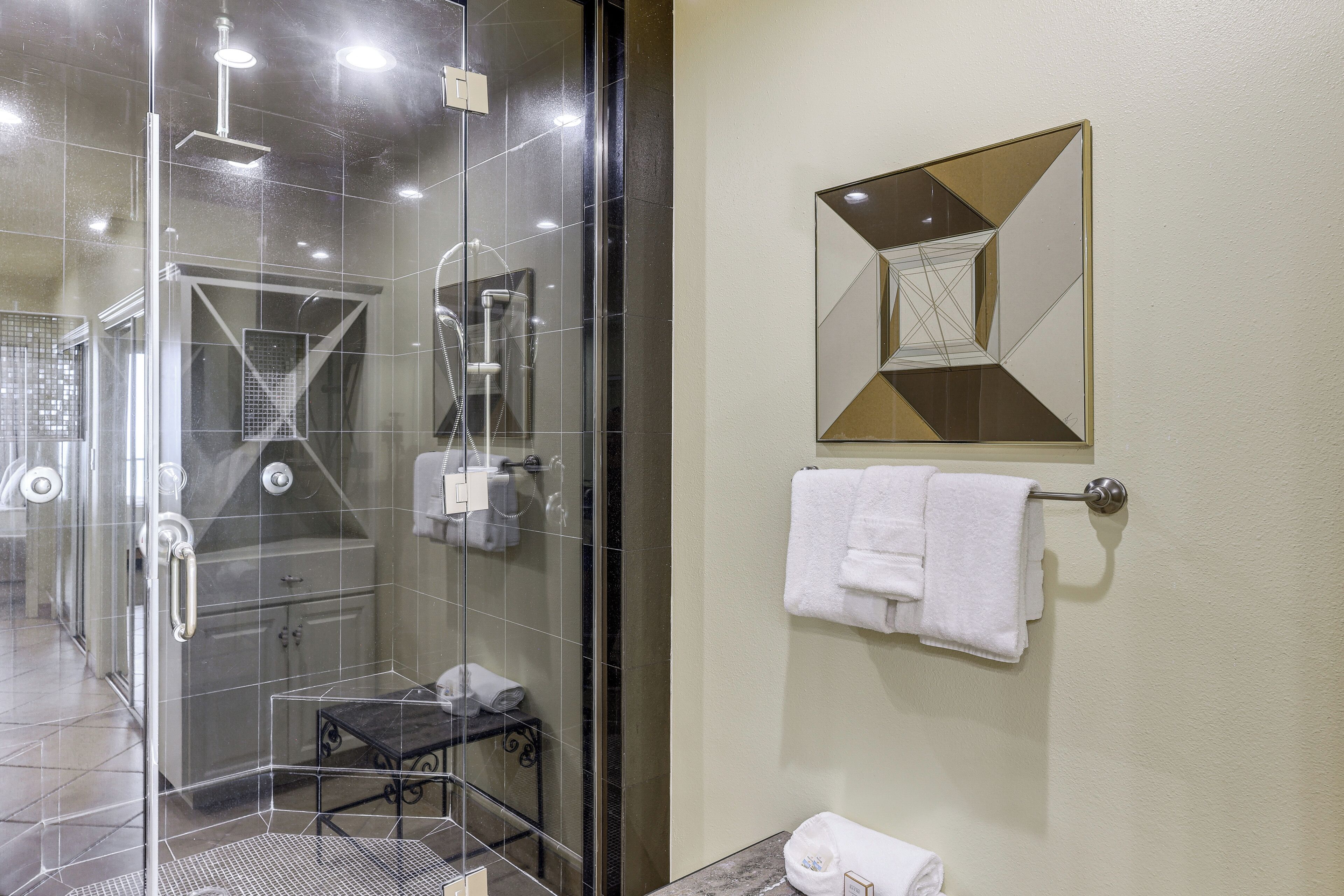 A modern bathroom with a glass-enclosed shower, a towel rack, and a decorative mirror.