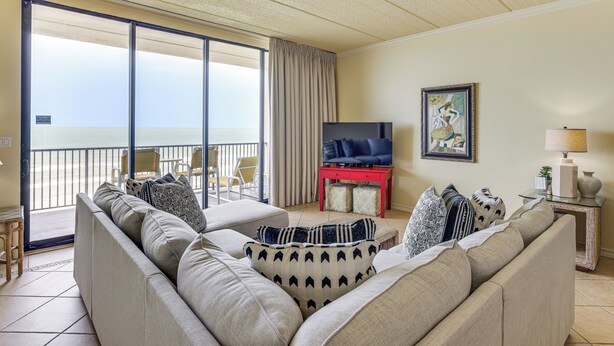 A living room with a sofa, television, and a balcony with a view. - 3BR Beachfront PH Suite: Suntide III - Unit 1203 (South Padre Island)