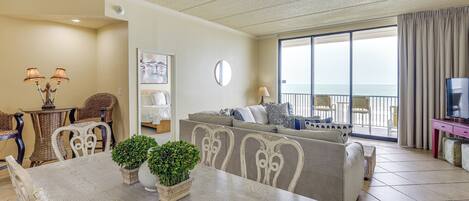 A living room with a dining table, chairs, a sofa, a TV, and a balcony with a view.