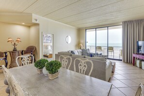 Ein Wohnzimmer mit Esstisch, Stühlen, einer Couch, einem Fernseher und einem Balkon mit Blick.