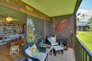 A room with wicker furniture, a glass door leading to a kitchen, and a view of a green lawn.