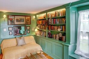 Ein Zimmer mit einem Bett, einem Bücherregal, gerahmten Bildern und einem Fenster mit Vorhängen.