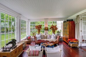 A room with a large window, a wooden cabinet, a sofa, and a wicker chair.