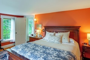 A bedroom with a large bed, a nightstand, a lamp, and a window with curtains.