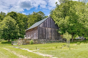 A rustic barn with a stone foundation, surrounded by lush greenery and trees.