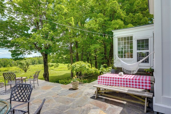 A patio with stone flooring, a hammock, a checkered table, and chairs.