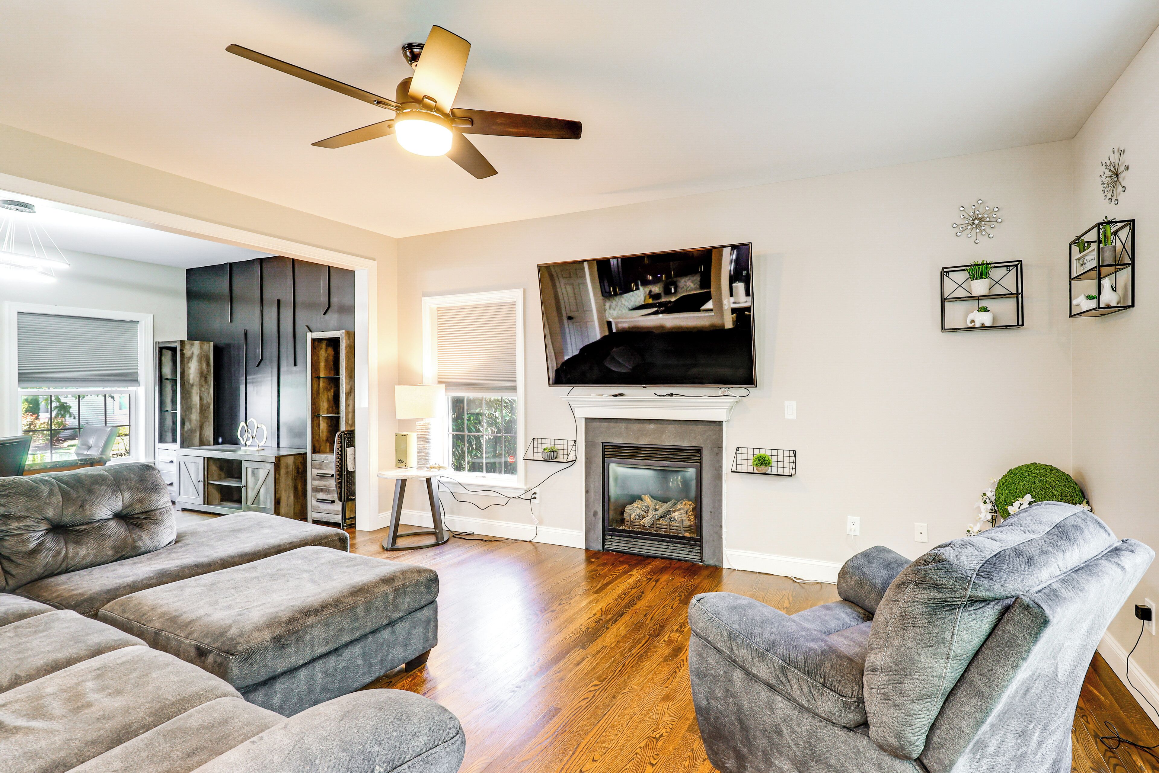 A living room with a fireplace, a ceiling fan, and a television mounted above it.