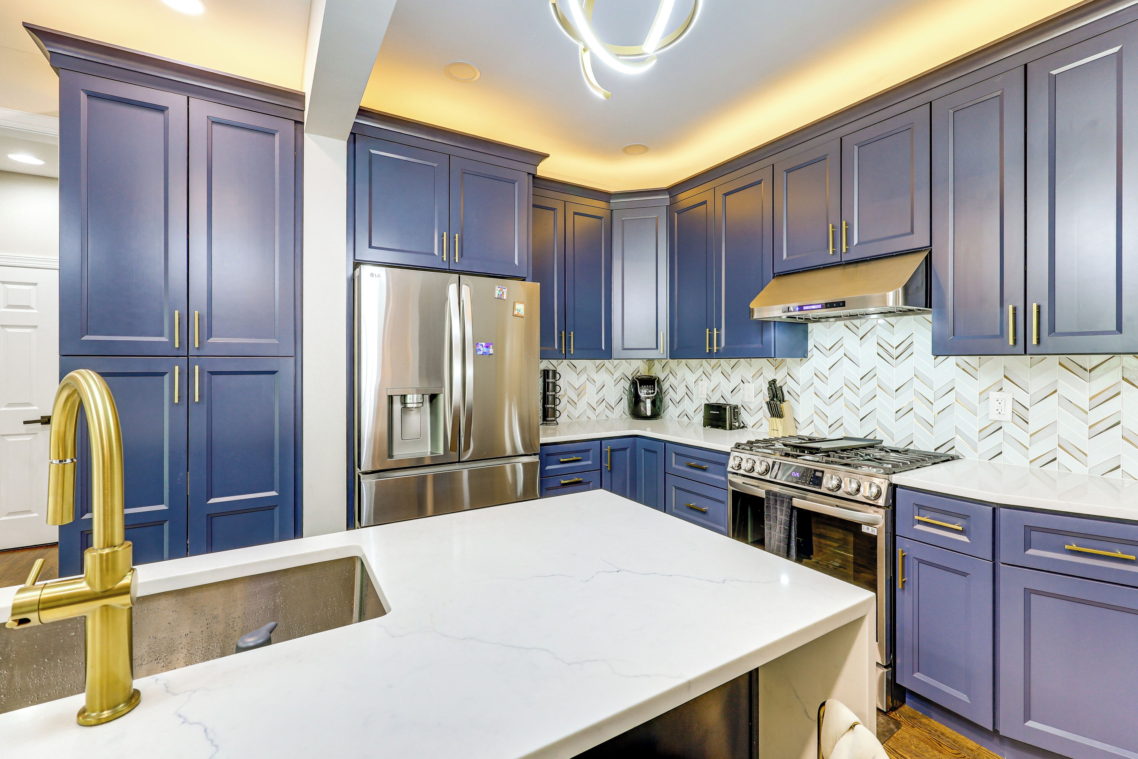 A kitchen with blue cabinets, stainless steel appliances, and a white marble countertop.