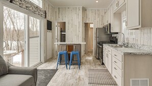 Una cocina con armarios blancos, encimera de granito y microondas empotrado. Hay dos taburetes azules y una ventana con vistas a un paisaje nevado.