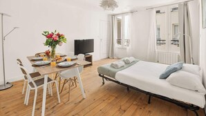 Ein Zimmer mit einem Bett, einem Esstisch mit Stühlen, einem Fernseher und einem Fenster mit Vorhängen.