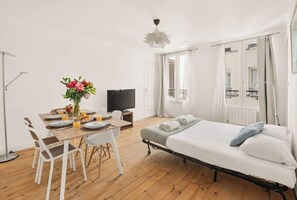 A room with a bed, a dining table with chairs, a TV, and a window with curtains. - Bright & Peaceful 2BR in Paris 10th (Paris)