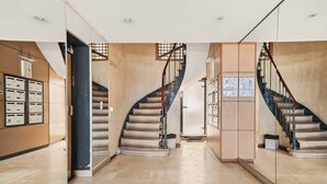 Ein modernes Interieur mit einer geschwungenen Treppe, einem Empfangsbereich mit Briefkästen und einem Gang mit Glastrennwand.