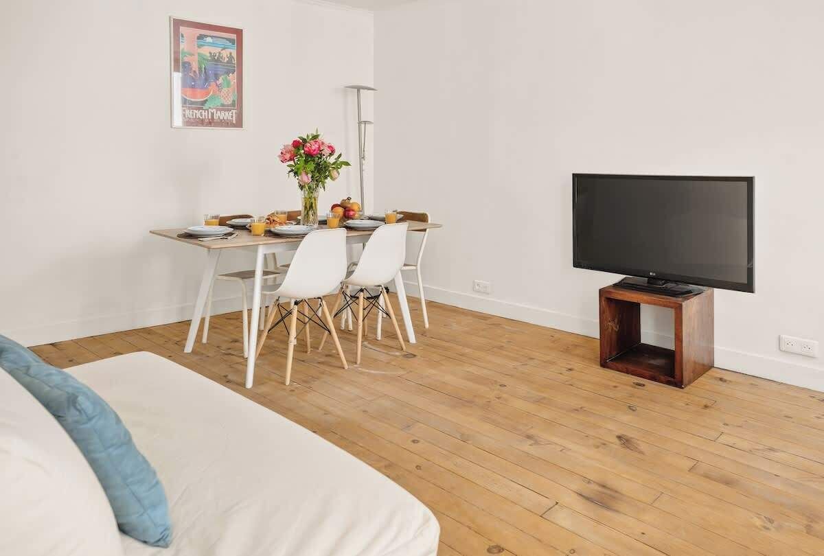 Een kamer met een bed, een eettafel met stoelen, een televisie op een dressoir en een poster aan de muur.