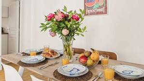 Ein Esstisch ist gedeckt mit Tellern, Gläsern und einer Obstschale. Im Hintergrund steht ein Blumenstrauß und ein Schild mit der Aufschrift Französischer Markt.