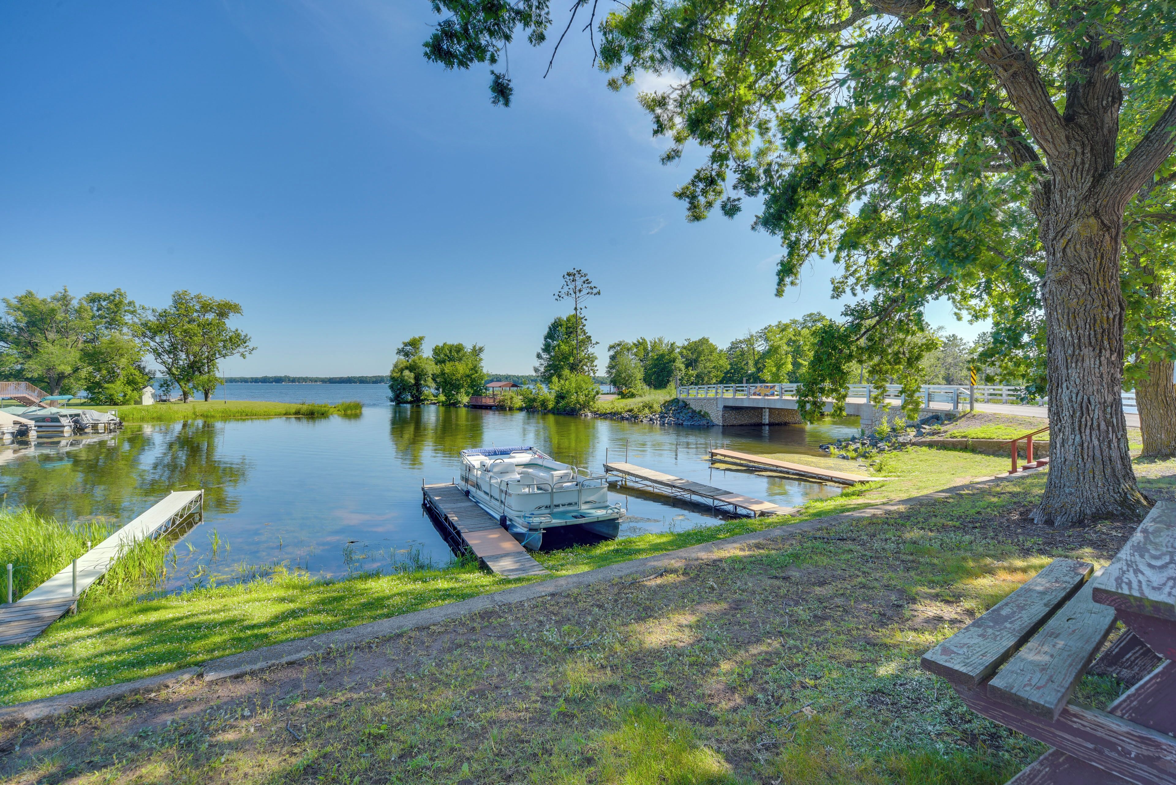 Une jetée au bord du lac avec des bateaux, un espace pique-nique et un pont enjambant l’eau.