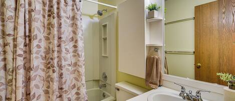 Een badkamer met douchegordijn, toilet, bad, wastafel, spiegel en een houten deur.