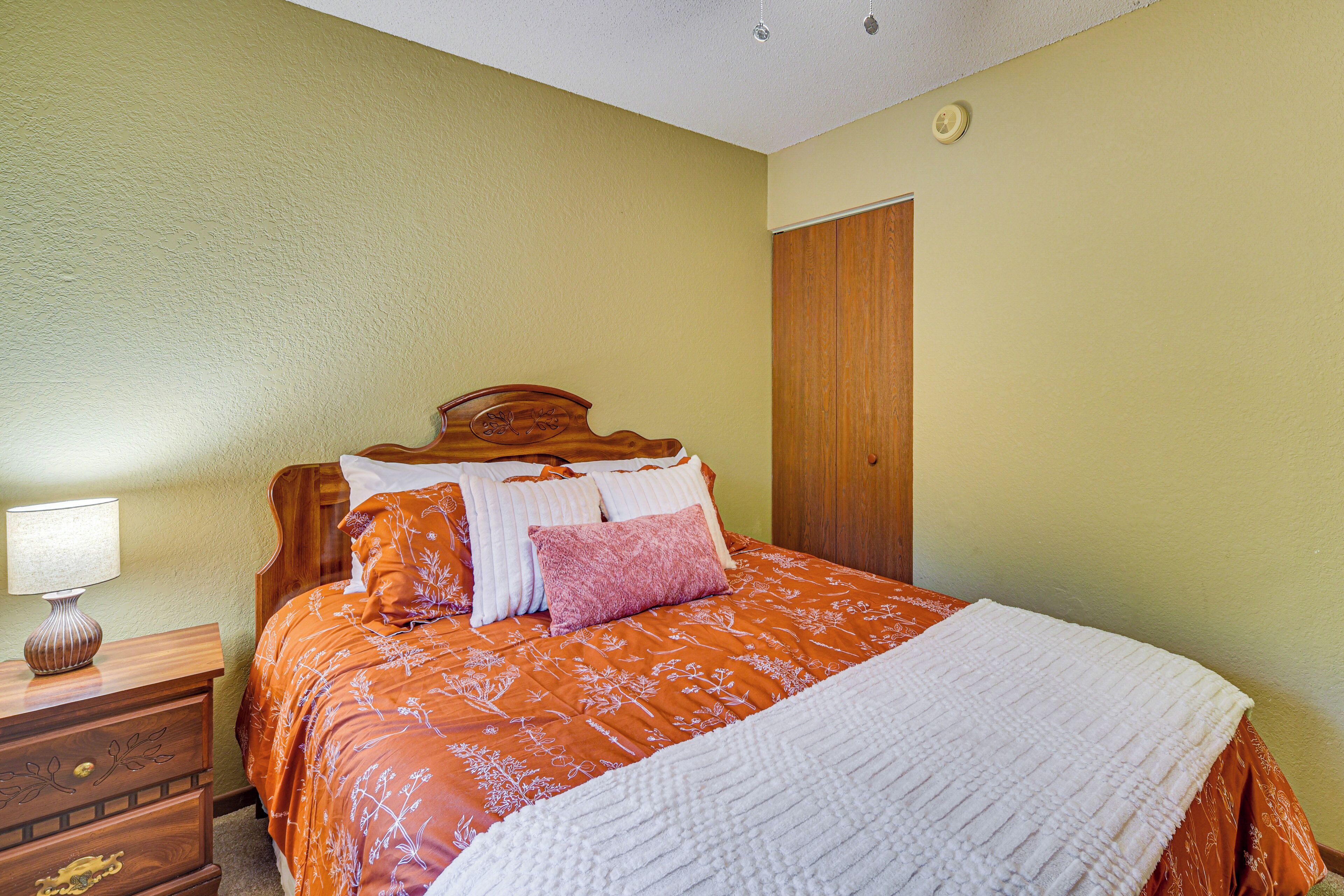 A bedroom with a bed, wooden headboard, nightstand, lamp, and a door.