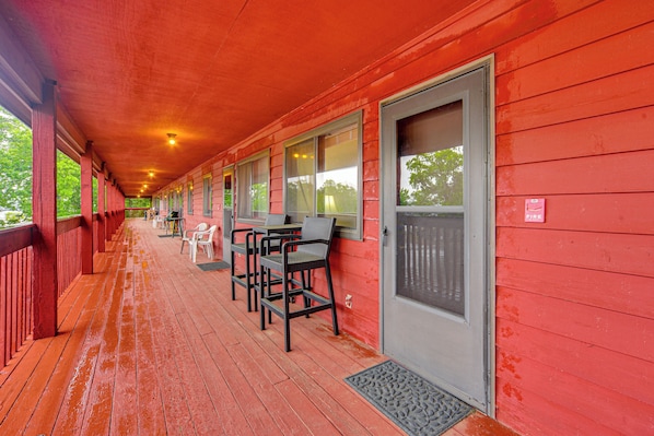 A covered porch with red siding, a door, and a window with a view of trees.