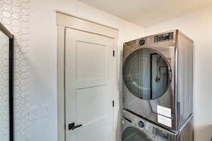 A laundry room with stacked washers and dryers, a white door, and a hexagonal tile wall.