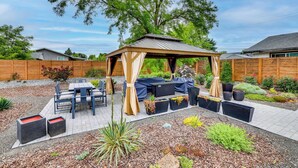 Ein überdachter Patio-Bereich mit Tisch und Stühlen, umgeben von Pflanzkübeln und einem Holzzaun.