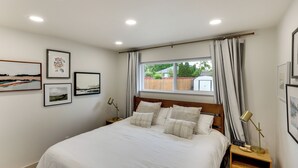 Ein ordentlich bezogenes Bett mit Kopfteil, ein Nachttisch mit Lampe und gerahmte Bilder an der Wand.