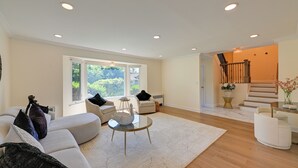 A spacious living room with a large window, a staircase, and a modern interior design. - Easy NYC Commute! Home 1 Mi to Dtwn Westbury (Westbury)