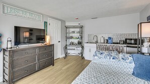 A bedroom with a bed, dresser, TV, kitchenette, and a sign reading 'Leisure Beach'. - Boat Dock Access! Pet-friendly Studio in Hudson (Hudson)